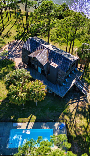 Aerial view of waterfront home with private pool surrounded by pines